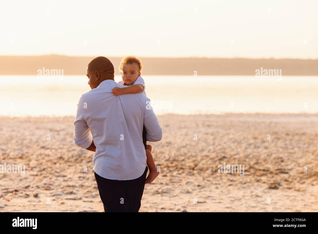 Un jeune père afro-américain marche sur la plage avec son tout-petit fils. Un bébé garçon sur les mains du père Banque D'Images