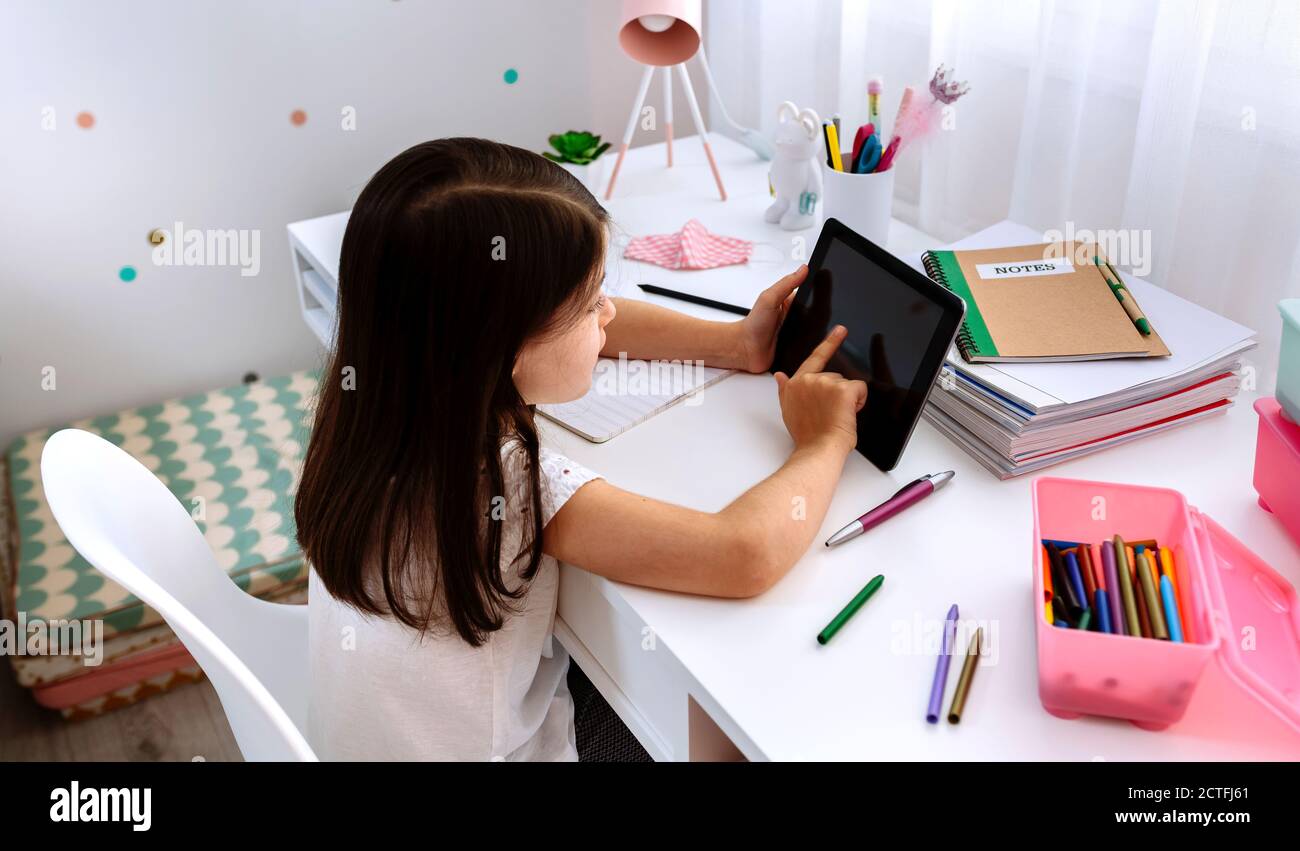 Fille étudiant à la maison avec un comprimé et un masque sur la table Banque D'Images