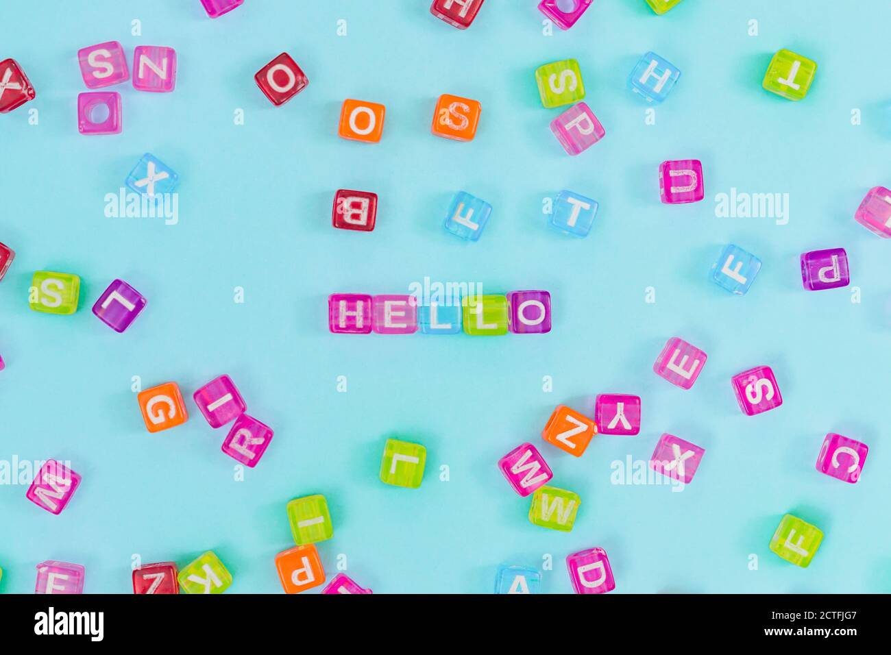 Perles cubes en plastique multicolore avec lettres éparpillées sur fond bleu et mots Bonjour. Texture d'arrière-plan alphabétique anglais Banque D'Images