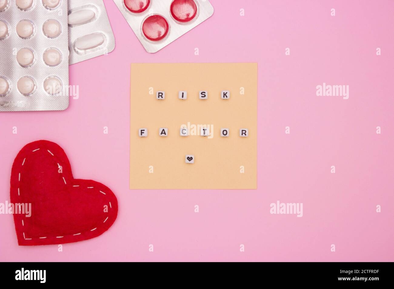 Concept de santé, cardiologie, maladie cardiaque. Mots FACTEUR DE RISQUE sur les cubes blancs, comprimés dans les cloques sur fond rose. Pose à plat. Banque D'Images