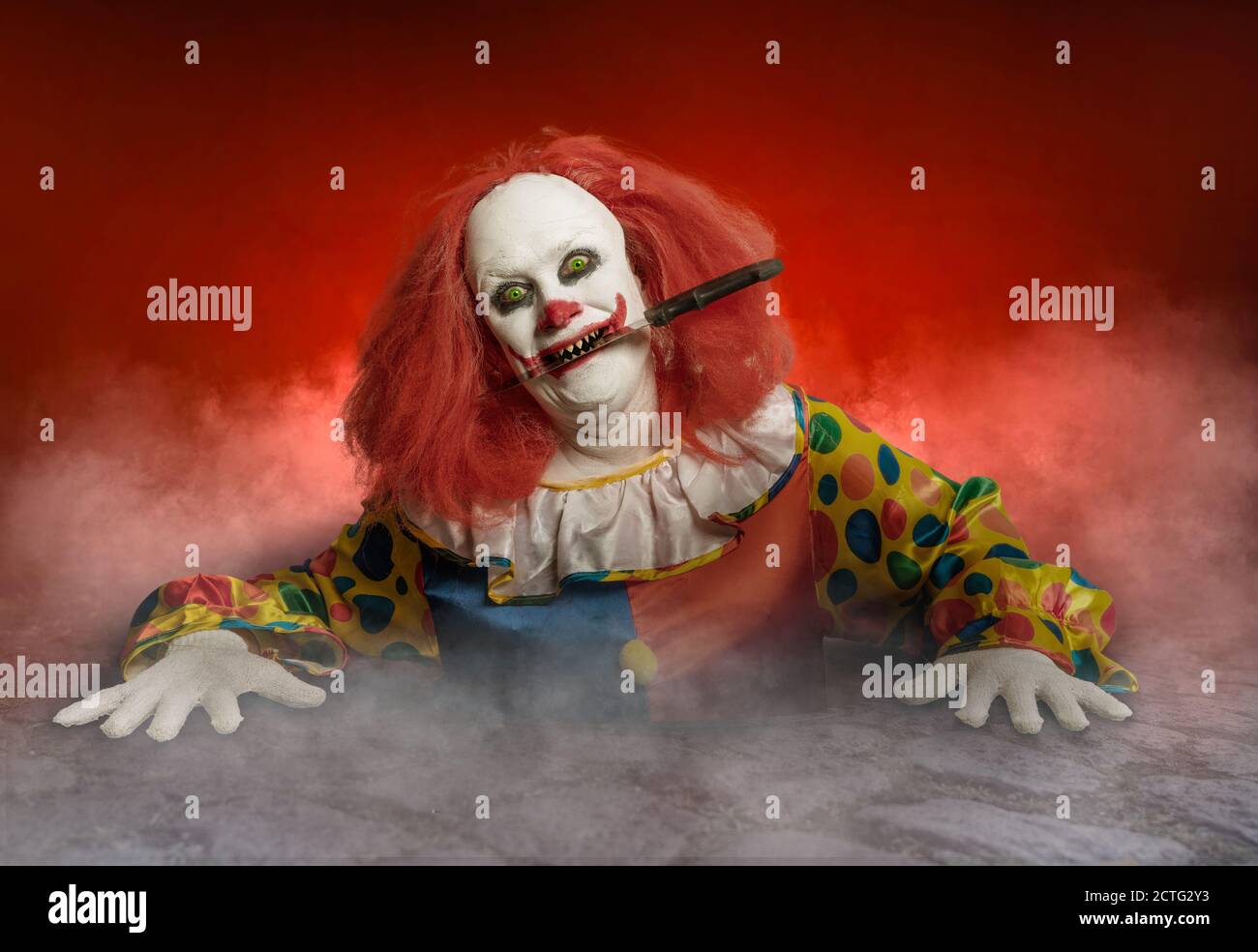 un clown effrayant avec un couteau dans la bouche levant de l'égout Banque D'Images