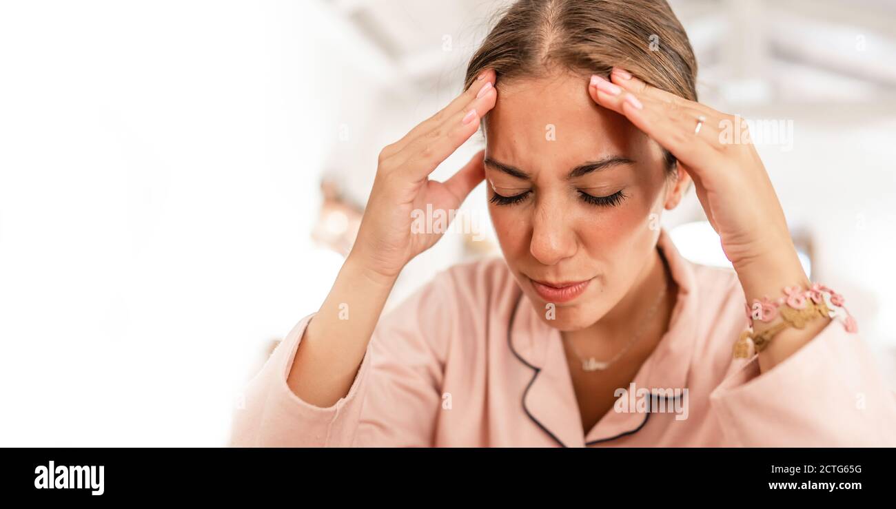 Une jeune femme du caucase portant un pyjama rose tient la tête dans ses mains et grimaces dans la douleur de la migraine maux de tête Banque D'Images