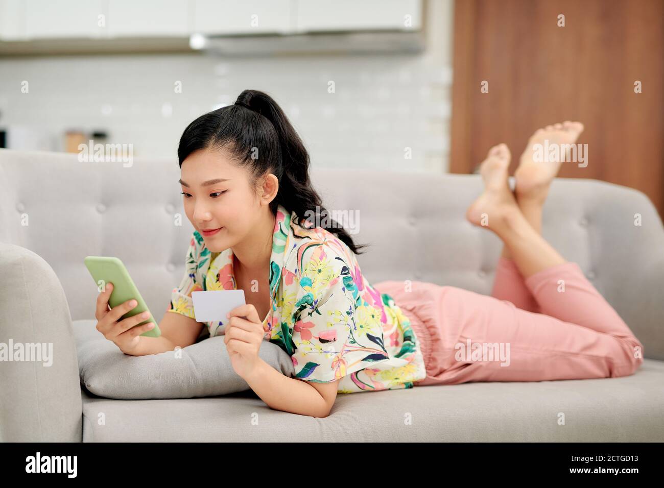 Photo d'une belle jeune femme surpris de brunette sur un canapé à l'intérieur à la maison en utilisant le téléphone portable tenant la carte de crédit. Banque D'Images