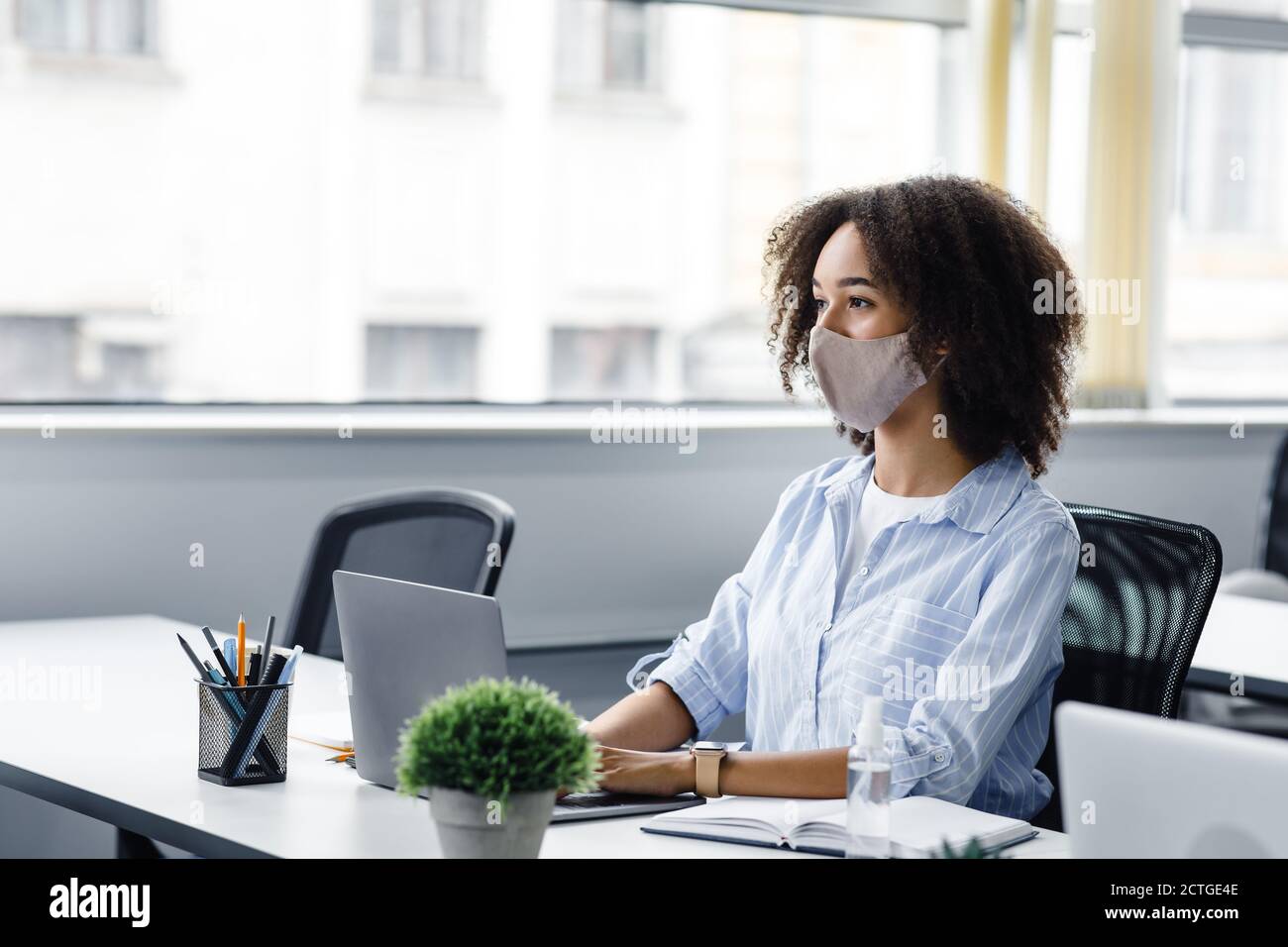 Un lieu de travail où travailler en collaboration. Une dame afro-américaine en masque de protection regarde le client ou un collègue et travaille dans un ordinateur portable, assis à une table avec un ordinateur portable Banque D'Images