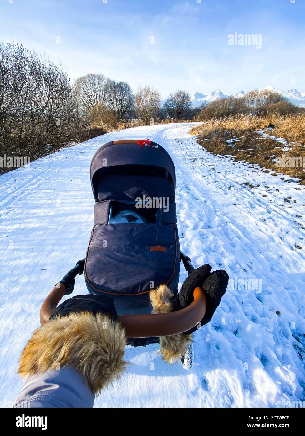 Vue grand angle de la main dans le gant en fourrure tenant bébé se balader sur un sentier enneigé avec des montagnes en arrière-plan en hiver Banque D'Images