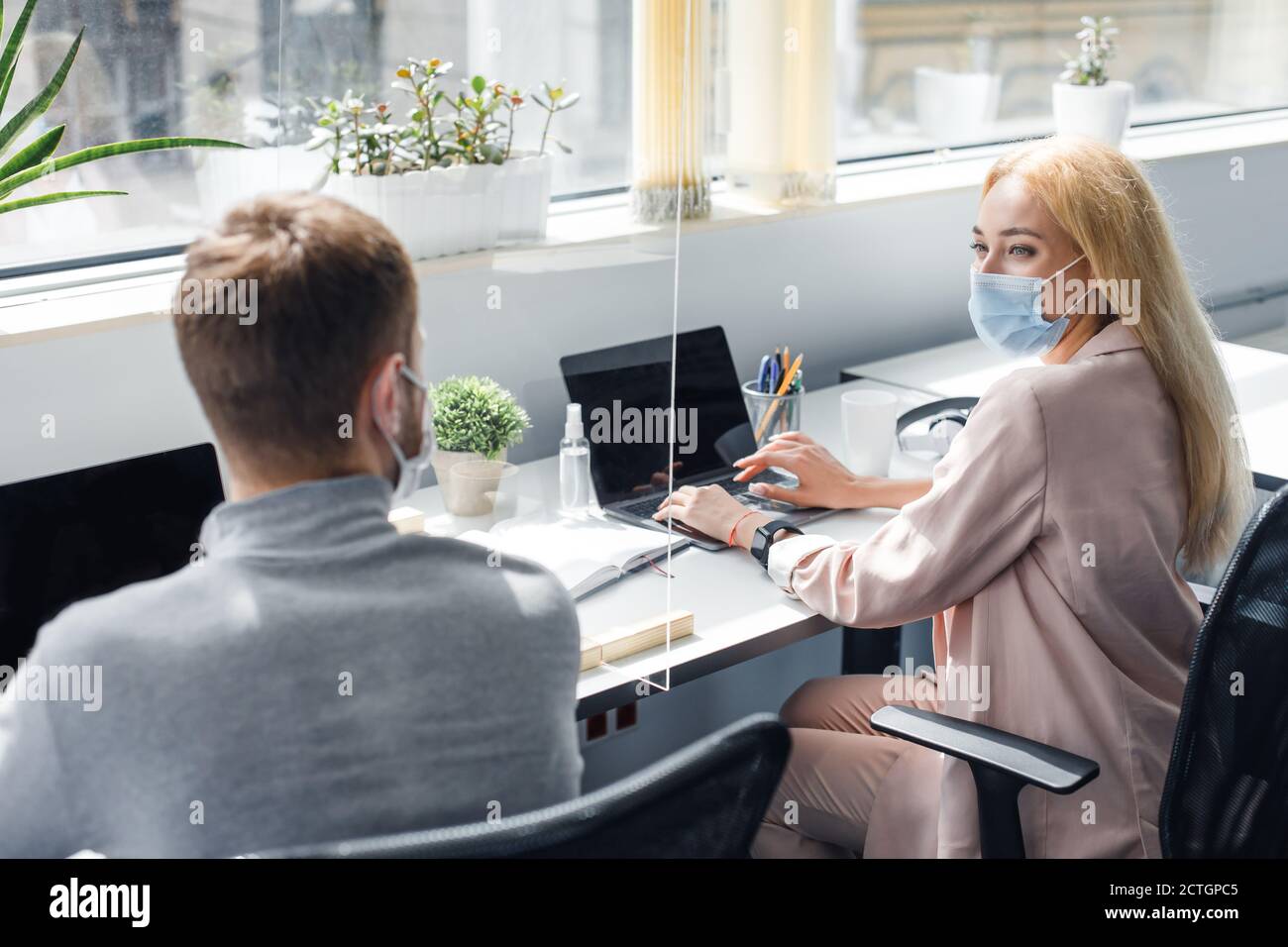 Nouvelle norme et communication des collègues par le biais du verre de verre. Un homme sympa et une dame qui travaillent sur des ordinateurs portables et qui parlent à l'intérieur du bureau Banque D'Images