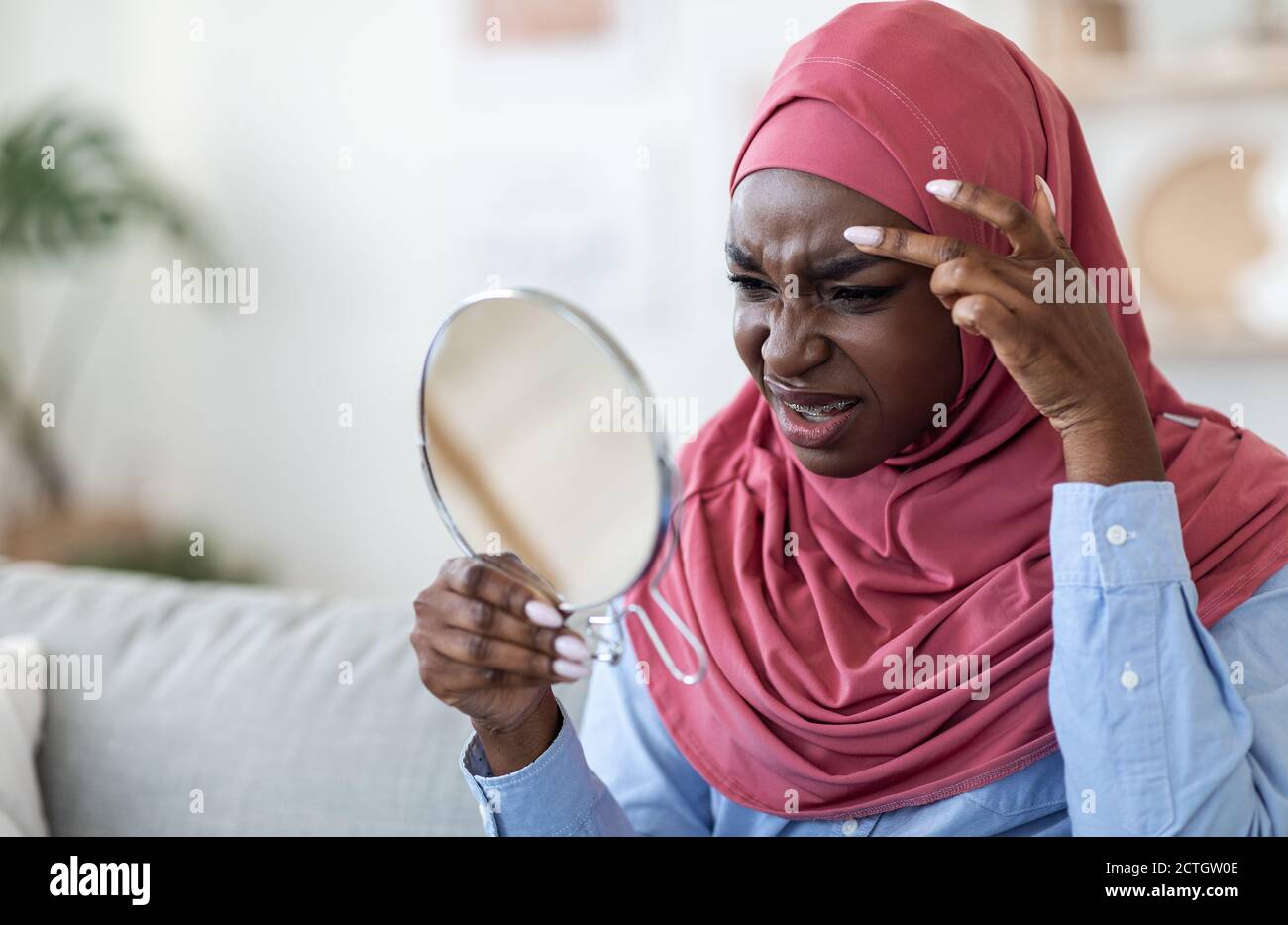 Problème de peau. Femme islamique noire dans le hijab regardant dans le miroir à la maison Banque D'Images