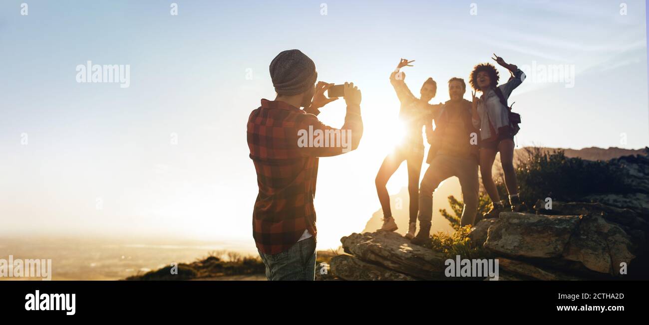 Groupe de randonneurs debout sur le sommet de la montagne photographiés par un ami. Homme photographiant ses amis sur la randonnée. Banque D'Images
