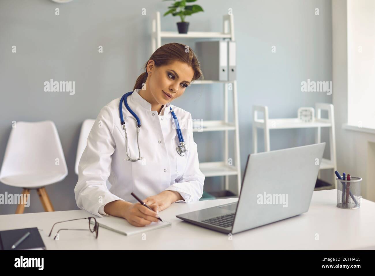 Femme médecin prenant des notes pendant une leçon en ligne ou un appel vidéo consultation en clinique médicale Banque D'Images