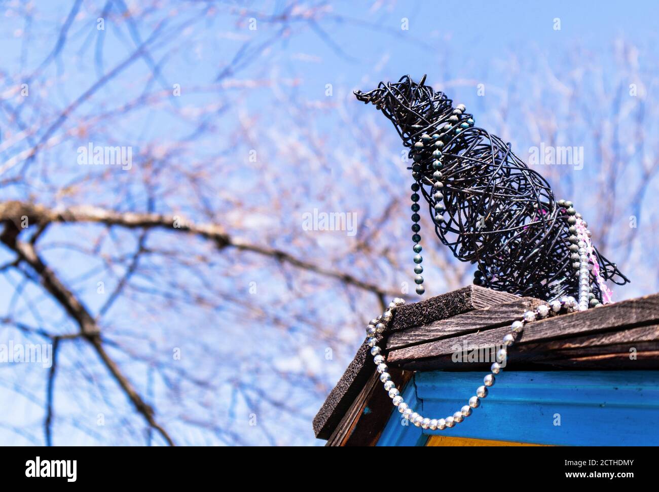 Corbeau, corbeau ou magpie fait main sur le toit. L'oiseau est fait de fil noir et de bijoux (collier de perles). Il est assis sur des bardeaux de toit avec du si bleu Banque D'Images