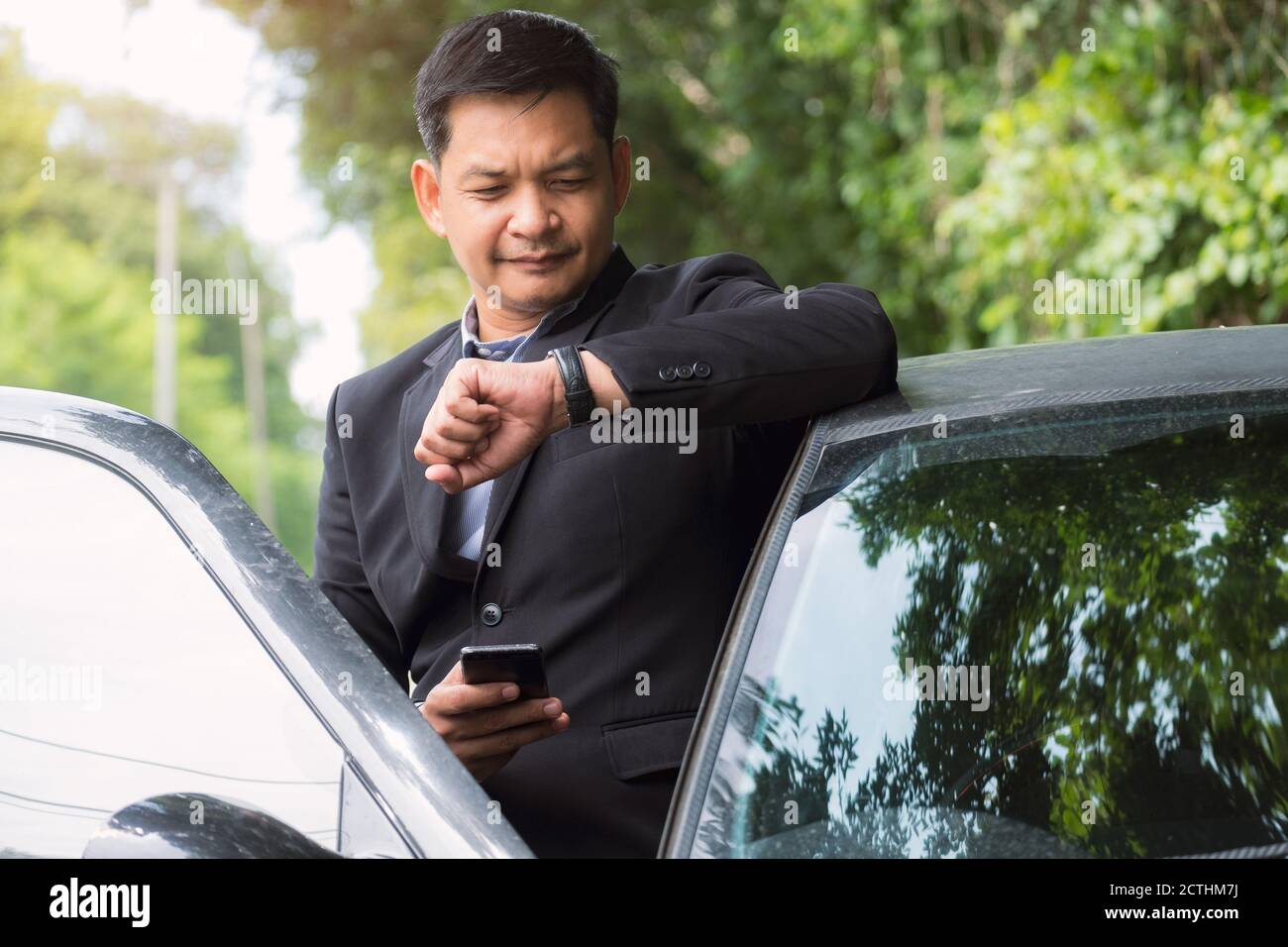 Portrait d'homme d'affaires portant un costume et regardant le temps debout près de sa voiture Banque D'Images