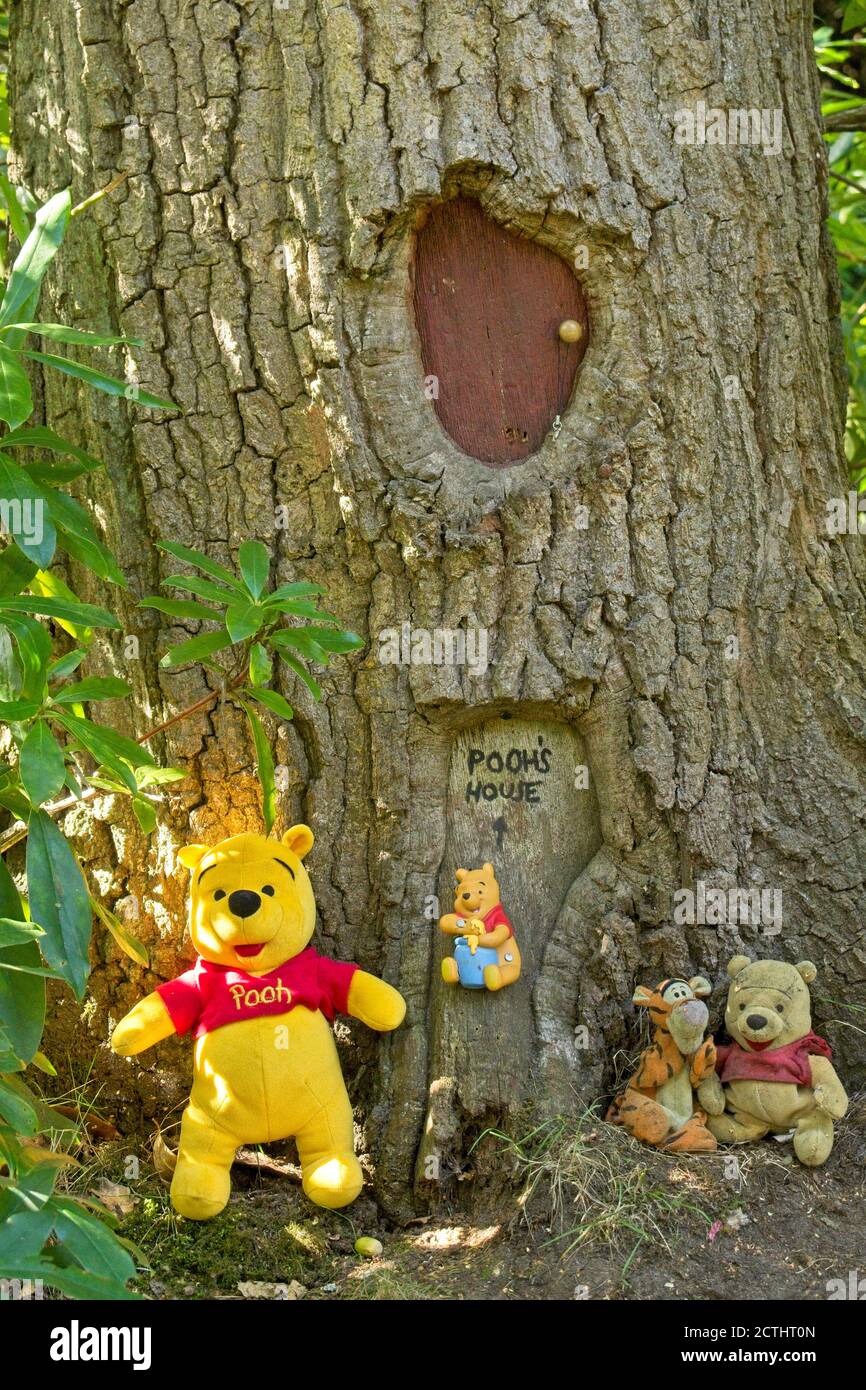 Effigie de Winnie l'Ourson et ses amis placés sur le sol à la base d'un  tronc d'arbre. Fenêtre et porte sculptées pour ressembler à la maison de la  forêt de pooh Photo