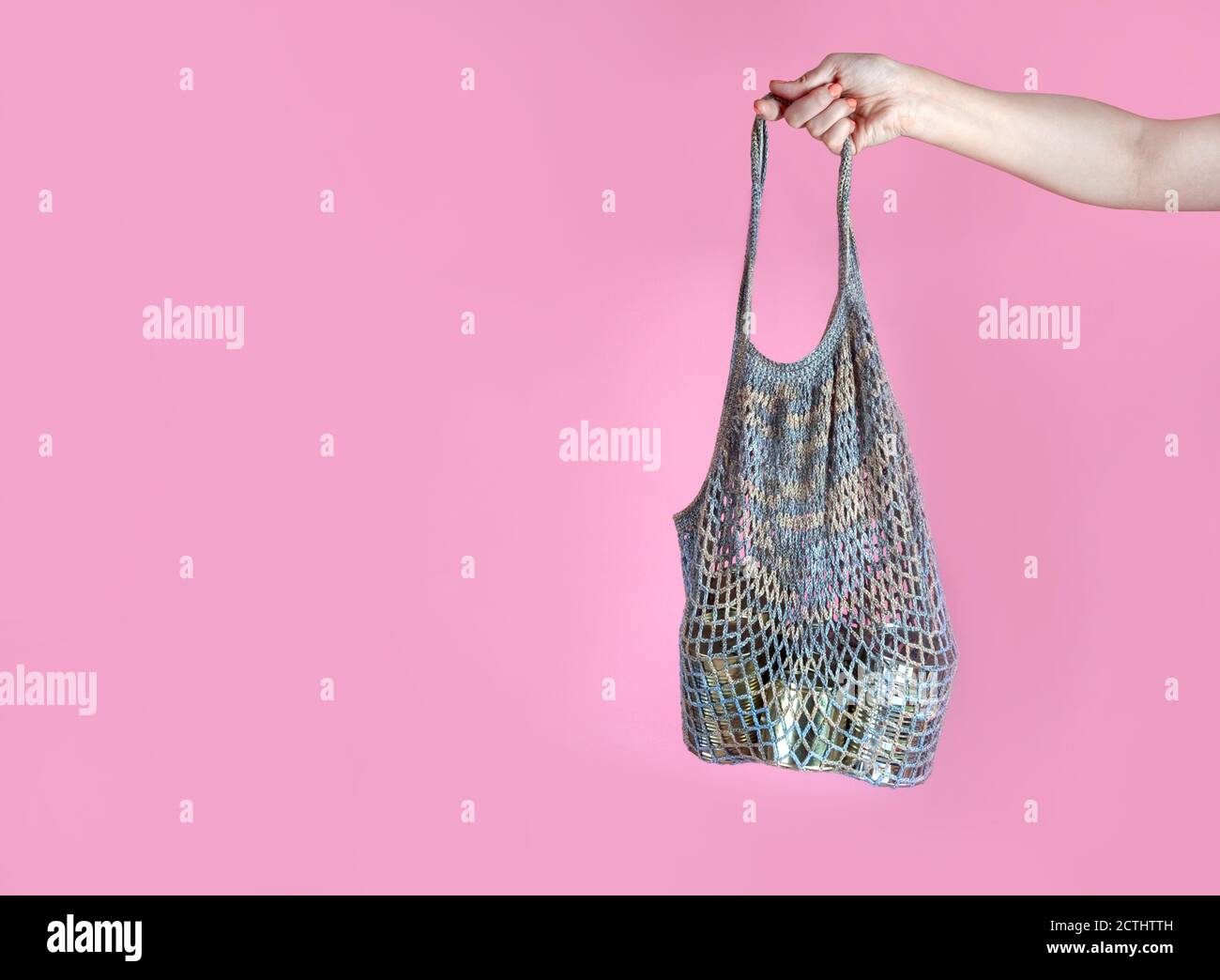 la main de la femme tient un sac à ficelle de crochet gris avec des boîtes en boîte, aide humanitaire, don de nourriture, sur un fond rose. Espace pour le texte Banque D'Images