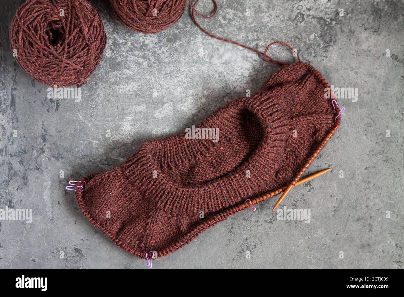 Chandail brun, procédé de tricotage, fond en béton. Aiguilles raglan. Fils tissés en laine. Banque D'Images