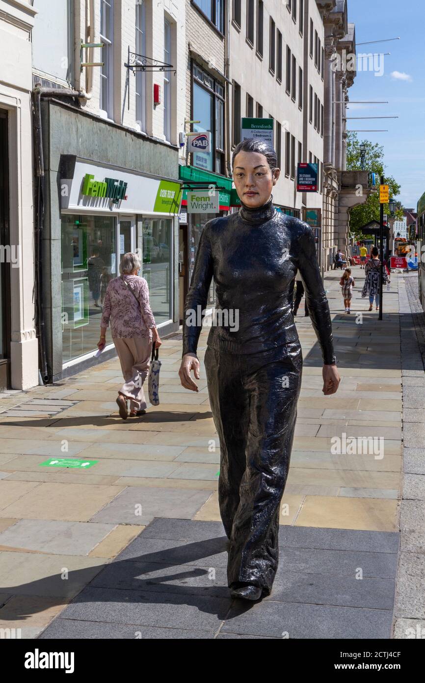 Une femme marchant le long de la rue, une des deux sculptures en bronze de Sean Henry, High Street, Colchester, Essex, Royaume-Uni. Banque D'Images
