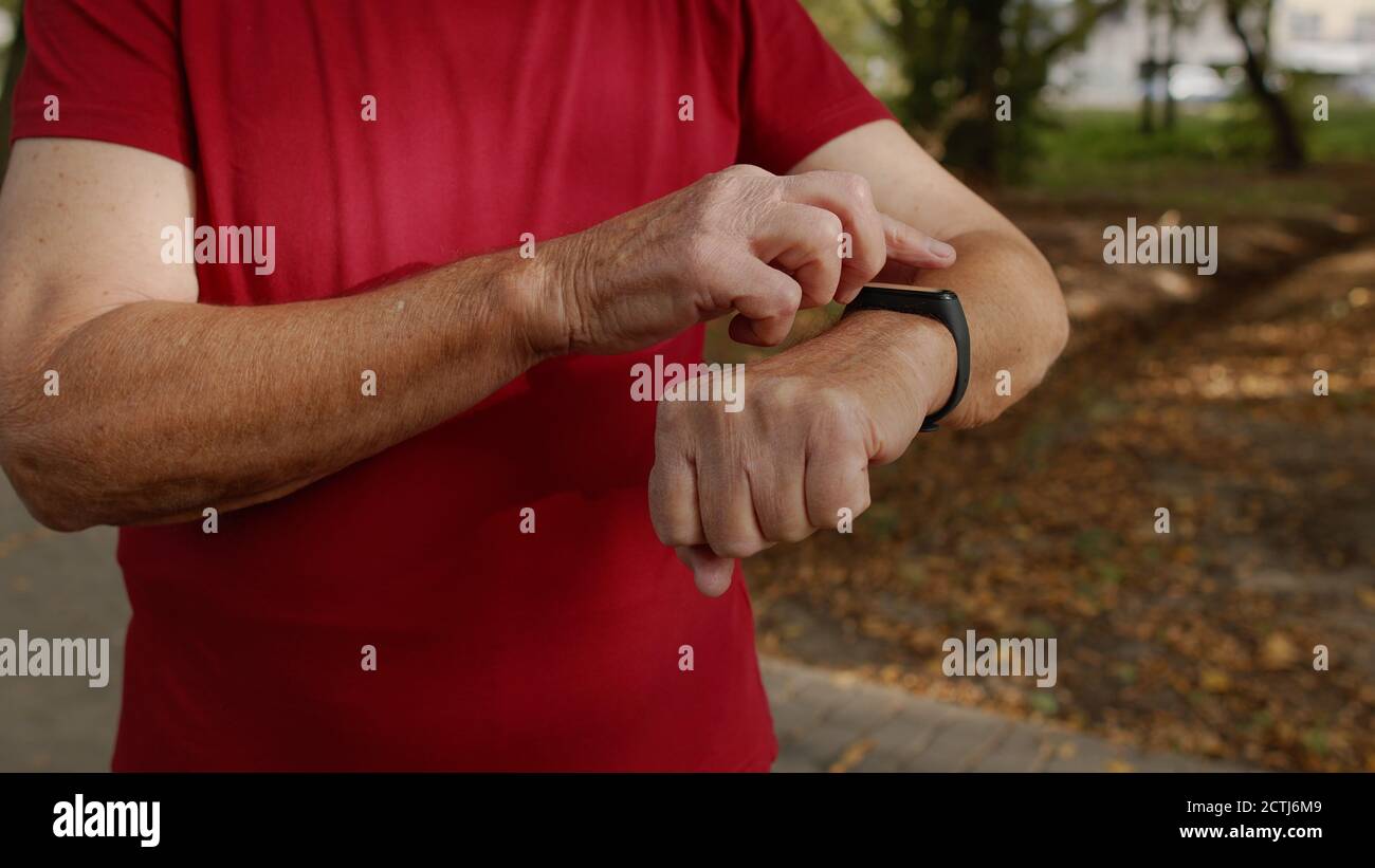 Ancien coureur débutant à toucher l'écran tactile de la montre intelligente, suivi de la distance, contrôle du pouls pendant l'entraînement physique. Moniteur de fréquence cardiaque avant le jogging. Concept de mode de vie sain Banque D'Images