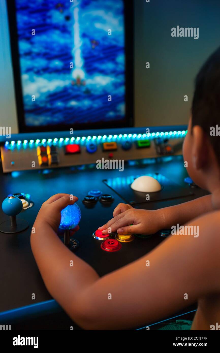 Gamin de quatre ans jouant à des jeux rétro sur une salle de jeux avec joystick lumineux et boutons sur un moniteur vertical. Banque D'Images