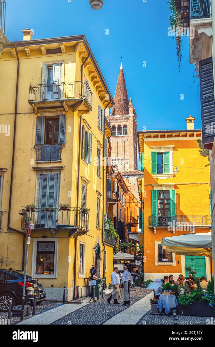 Vérone, Italie, 12 septembre 2019: Rue italienne typique avec des bâtiments traditionnels avec des fenêtres à volets, restaurant de rue, photo de style rétro, tour de la basilique de Santa Anastasia église Banque D'Images