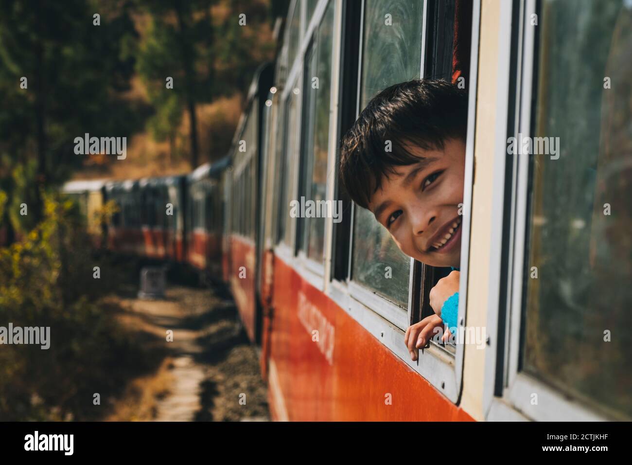 Jeune garçon souriant par la fenêtre du train de jouets, tandis que le train monte de Kalka à Shimla Banque D'Images