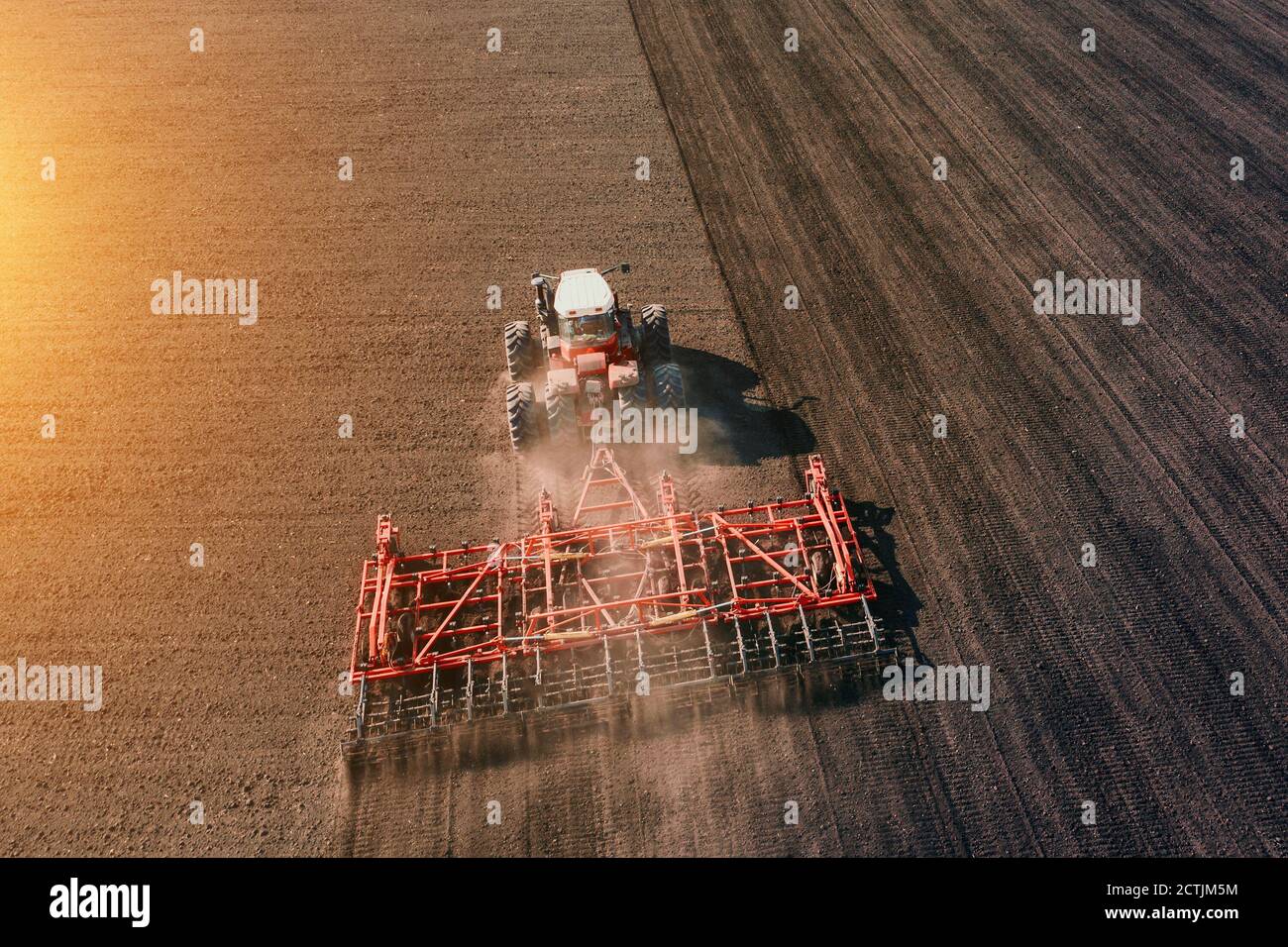 Tracteur cultivant ou labourant un champ agricole dans la lumière du coucher du soleil, vue aérienne. Banque D'Images