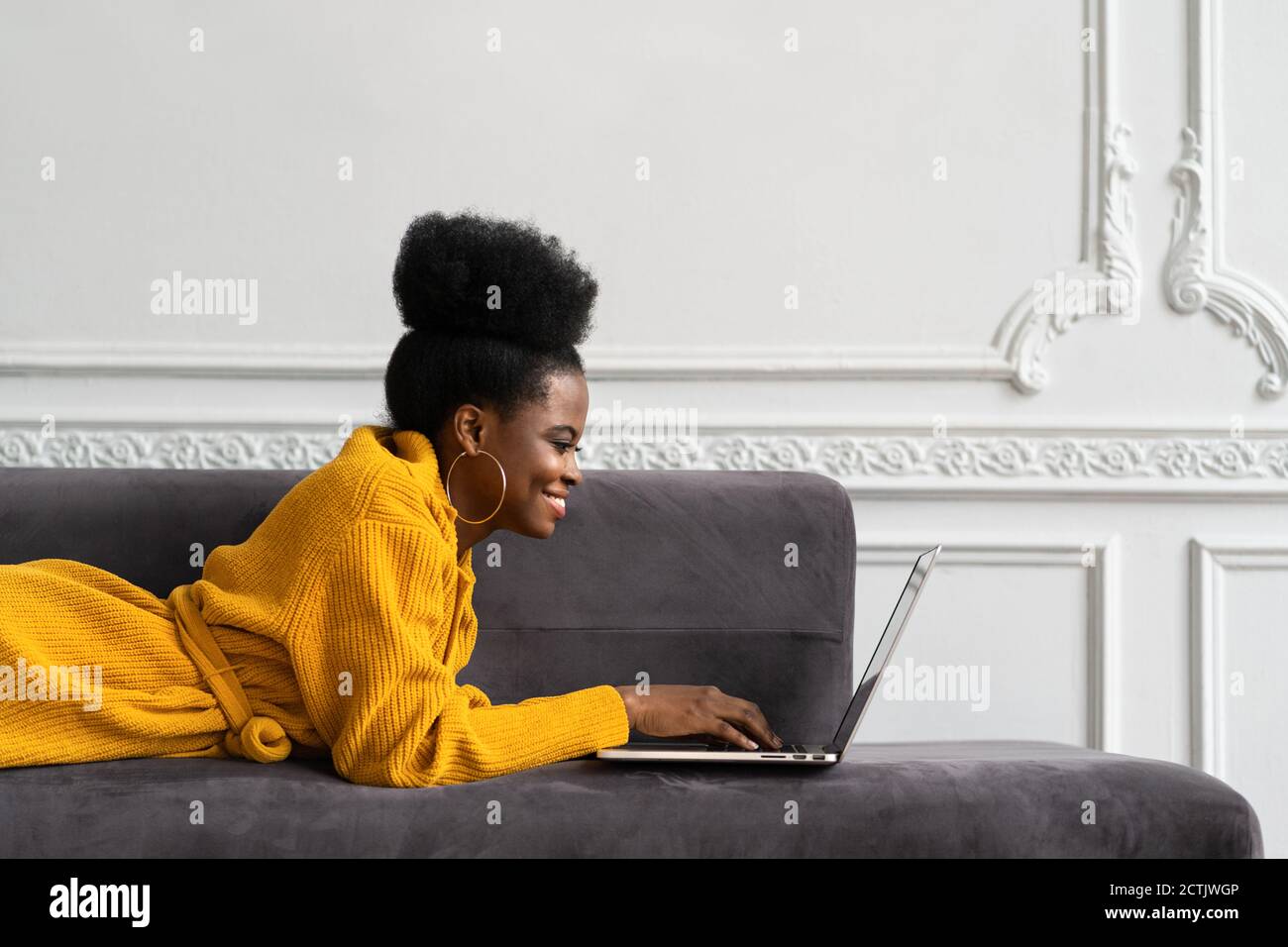 Gros plan de la femme biraciale afro-américaine souriante avec une coiffure afro-américaine dans un gilet jaune allongé sur un canapé, au repos, regardant la webcam de l'appareil photo et parlant Banque D'Images