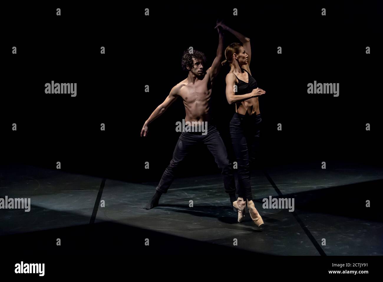 Danseuse féminine et masculine effectuant un ballet contemporain sur scène noire Banque D'Images