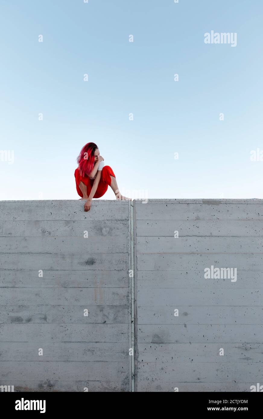 Une jeune femme qui se croque sur un mur contre un ciel clair Banque D'Images