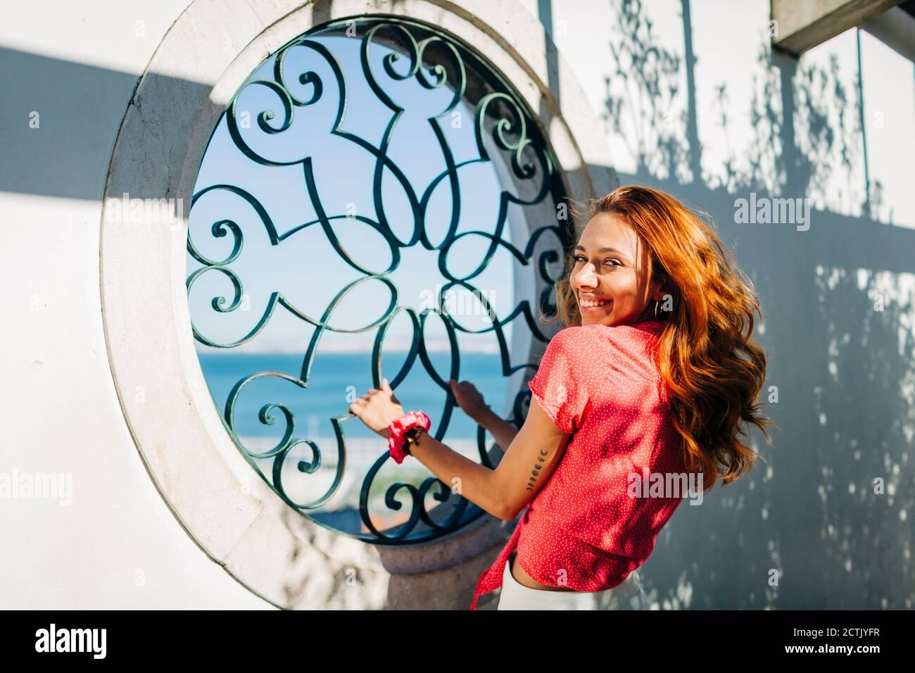 Jeune femme souriant tout en tenant une grille de fenêtre à Alfama, Lisbonne, Portugal Banque D'Images