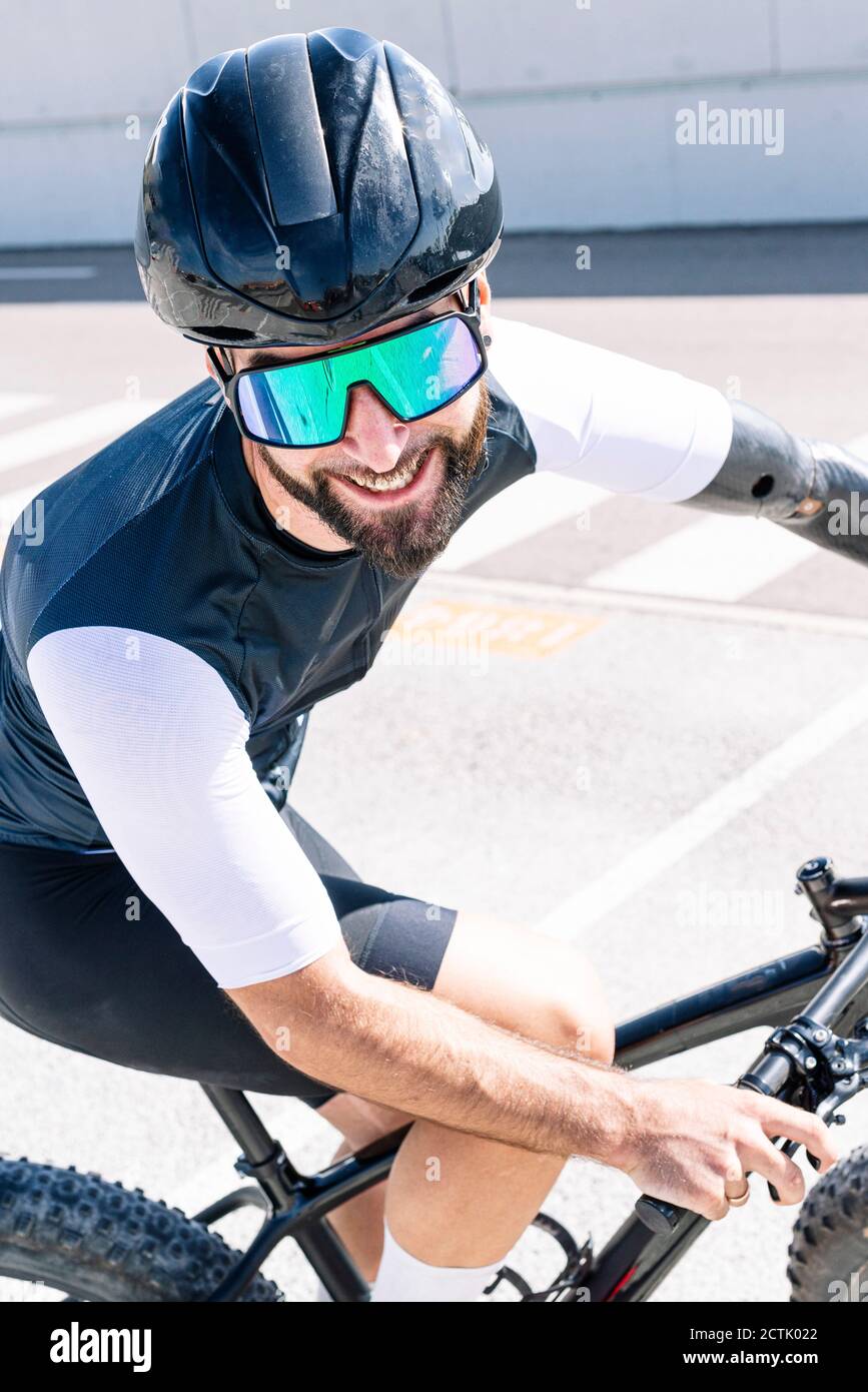 Gros plan d'un athlète en amputation souriant portant des lunettes de soleil tout en faisant du vélo sur route Banque D'Images