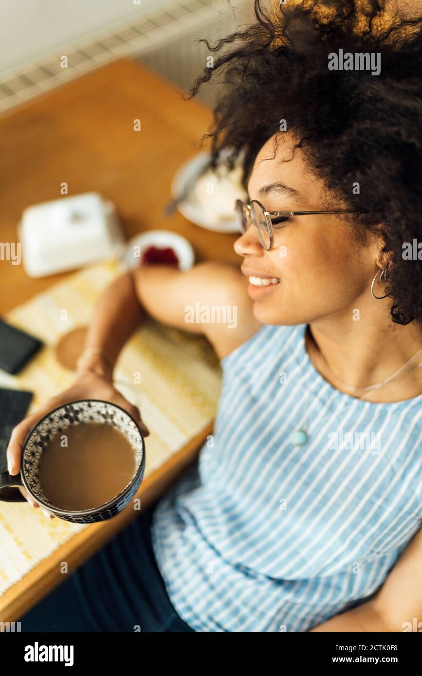 Gros plan de la jeune femme avec les yeux fermés tenant la tasse à café assis à la table Banque D'Images