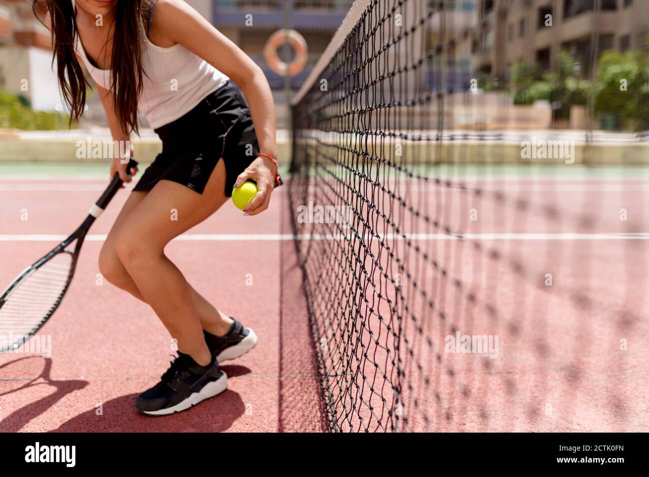Joueuse de tennis féminine tenant la raquette et le ballon tout en restant debout filet dans le court Banque D'Images