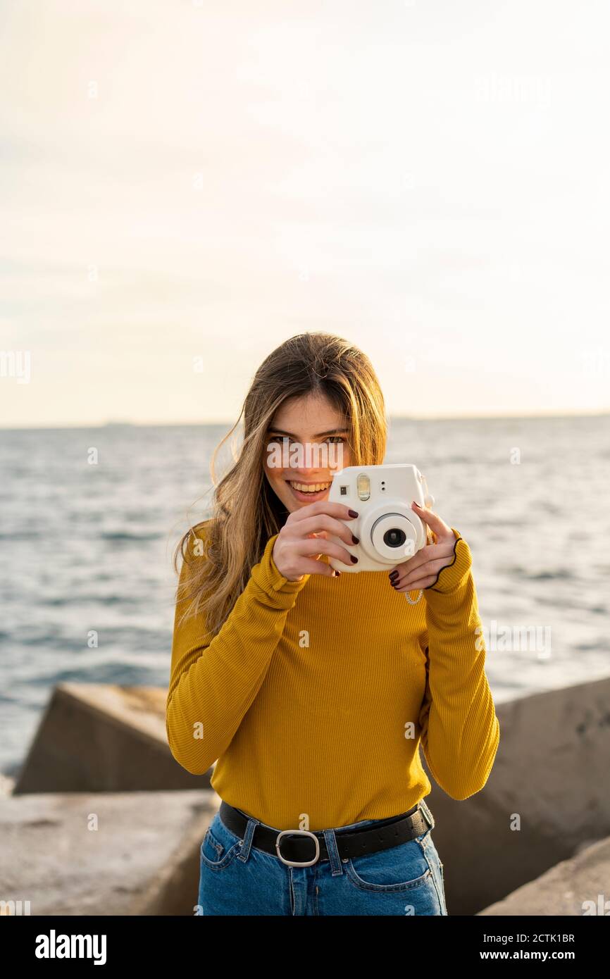 Femme souriante avec appareil photo debout contre la mer Banque D'Images