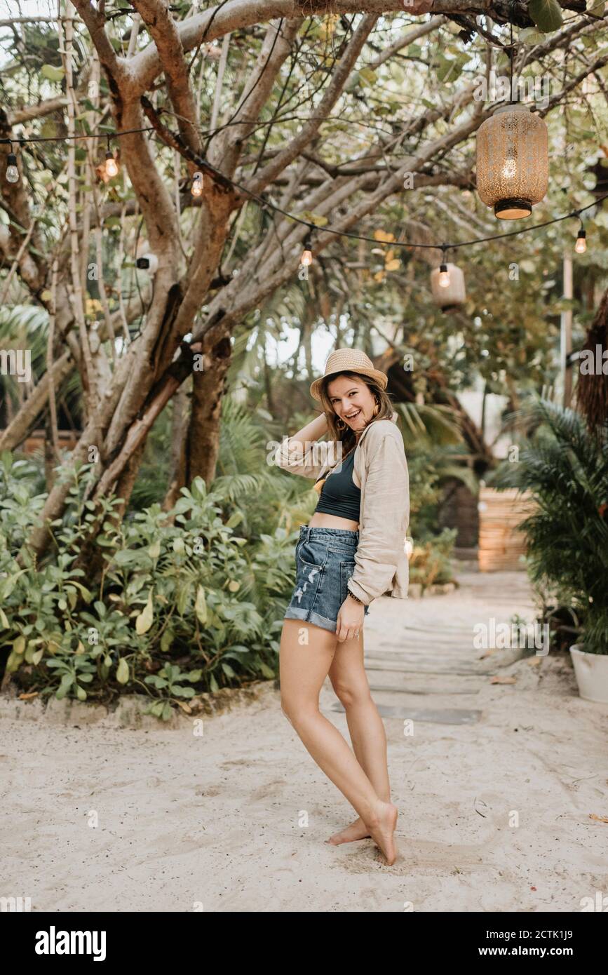 Femme souriante avec chapeau posé devant l'arbre Banque D'Images