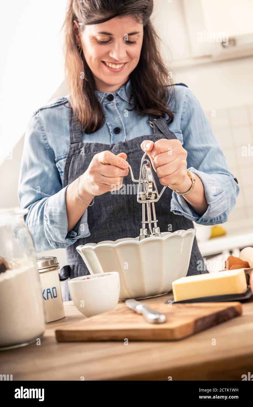 Femme souriante utilisant un tire-paille tout en se tenant dans la cuisine à accueil Banque D'Images