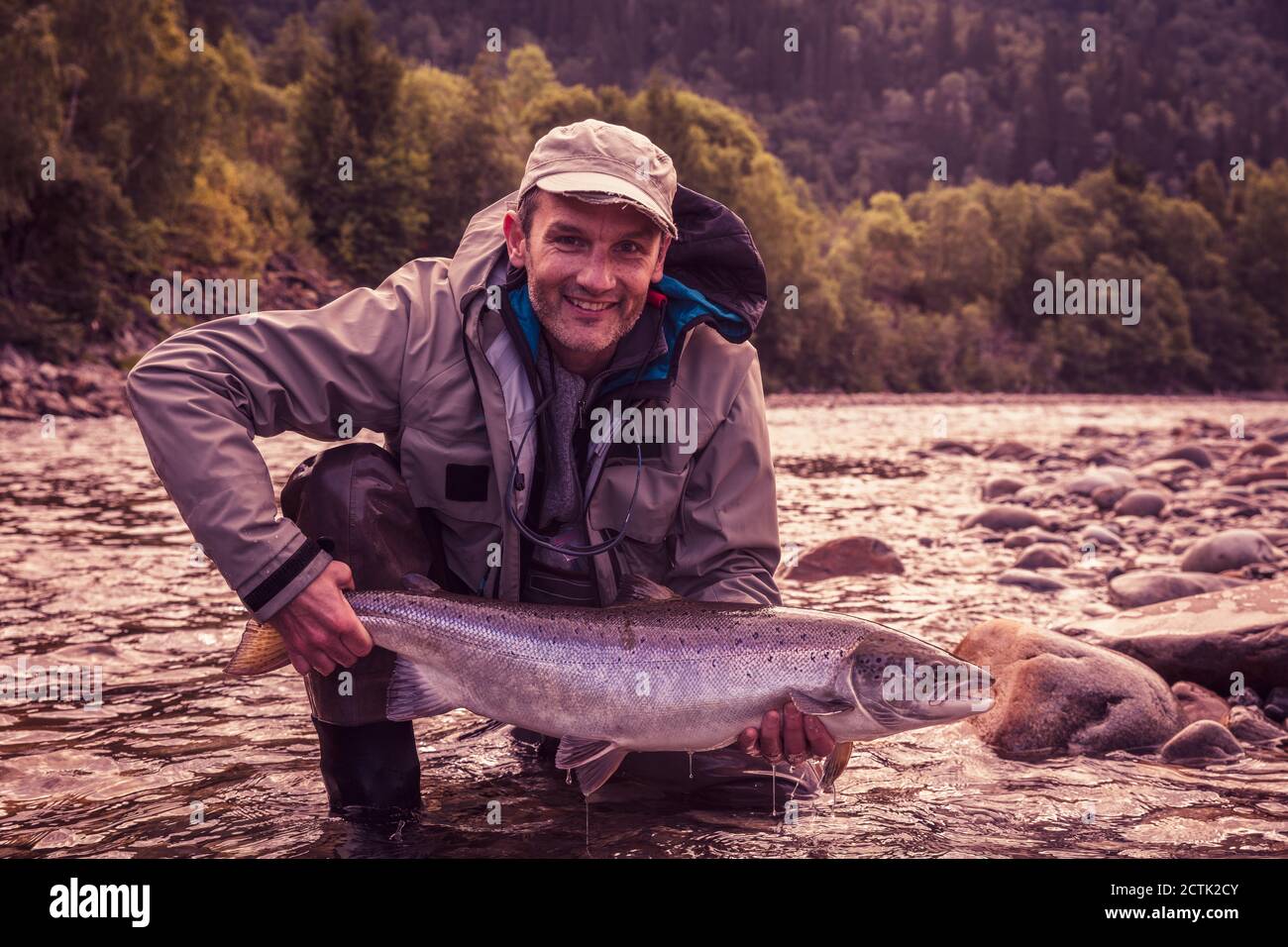 Faites voler le pêcheur en souriant tout en tenant le saumon pêché dans la rivière Banque D'Images