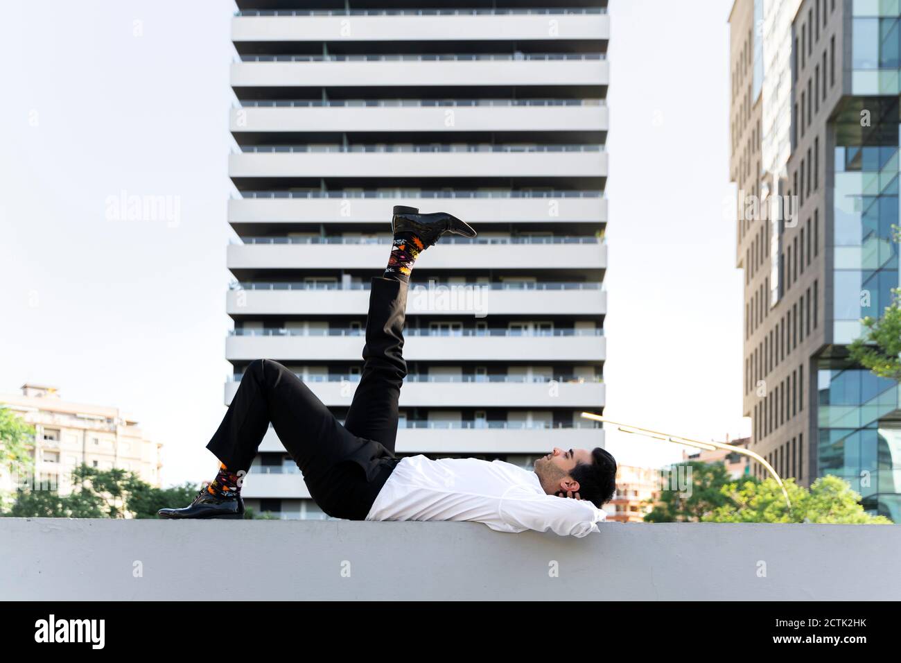 Homme d'affaires avec le pied couché sur le mur de retenue contre moderne bâtiment en ville Banque D'Images
