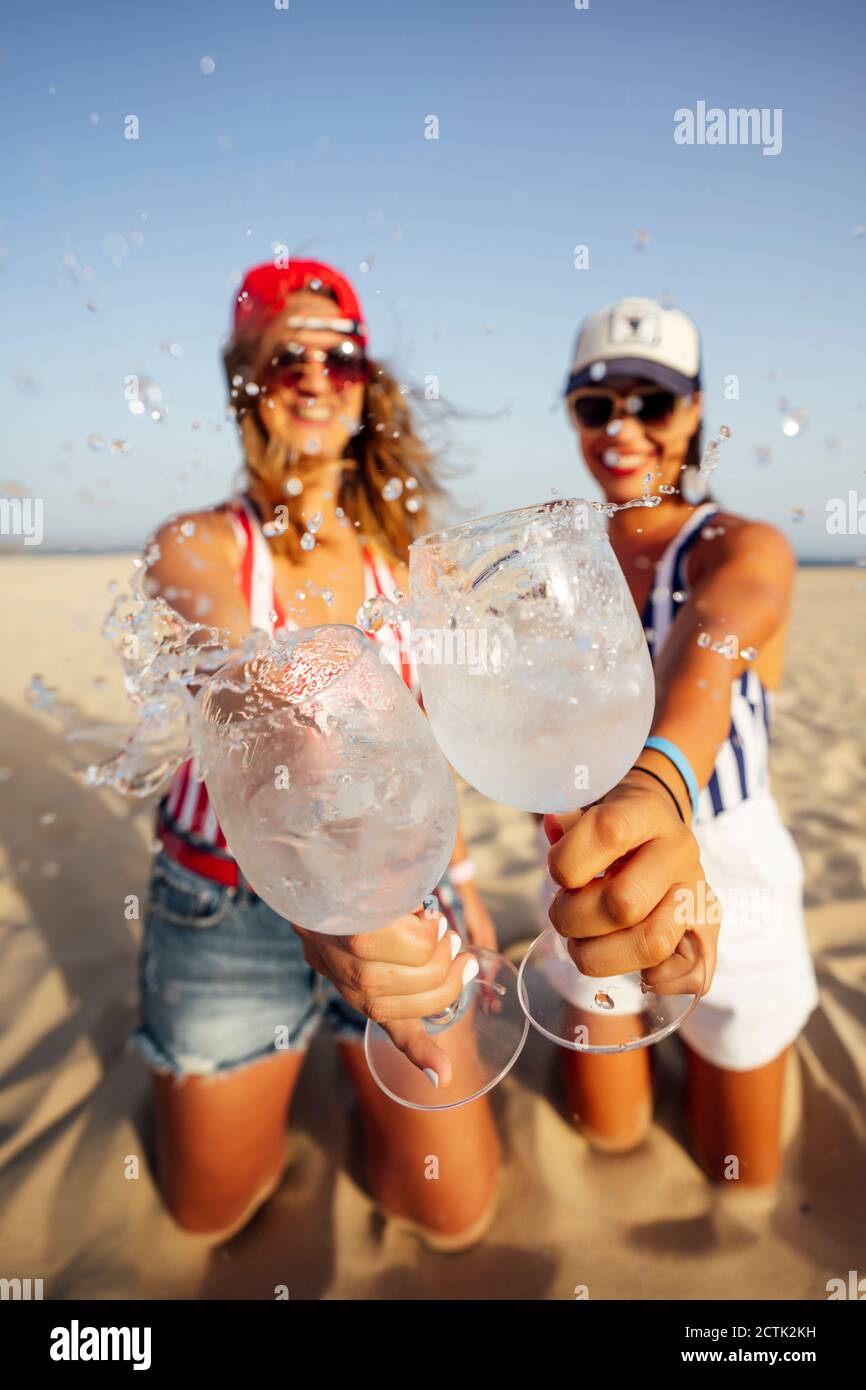 De joyeuses amies qui barbotent en buvant un verre tout en dorant à la plage jour ensoleillé Banque D'Images