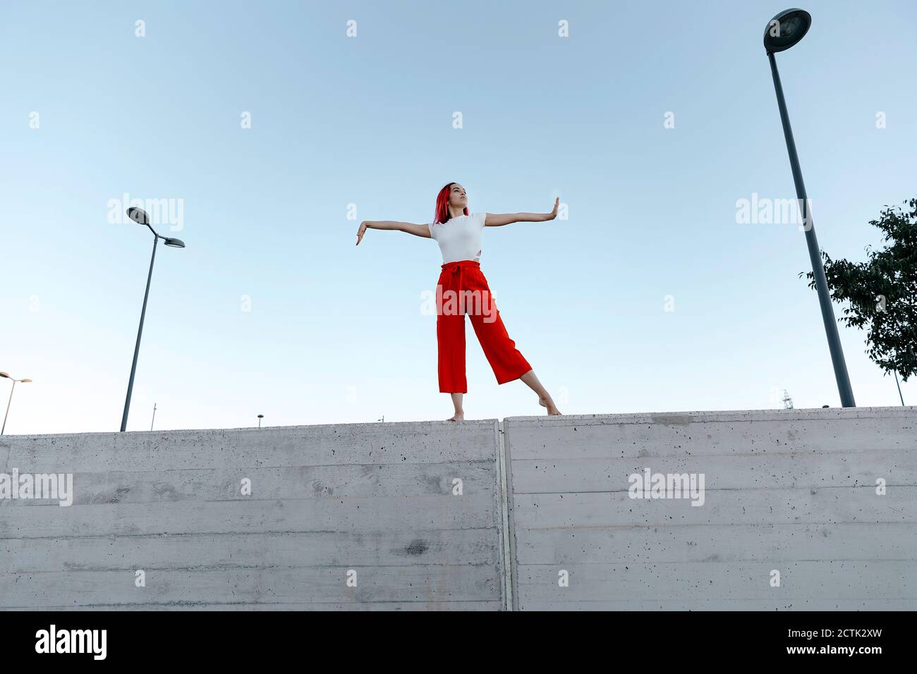 Jeune danseur avec bras tendus debout sur le mur environnant contre ciel dégagé Banque D'Images
