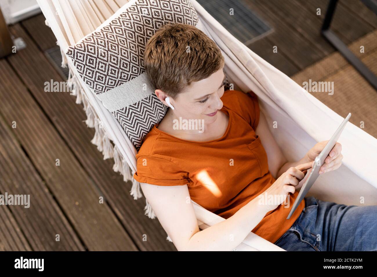 Femme adulte de taille moyenne avec cheveux courts utilisant la tablette numérique pendant sur hamac sur le porche Banque D'Images