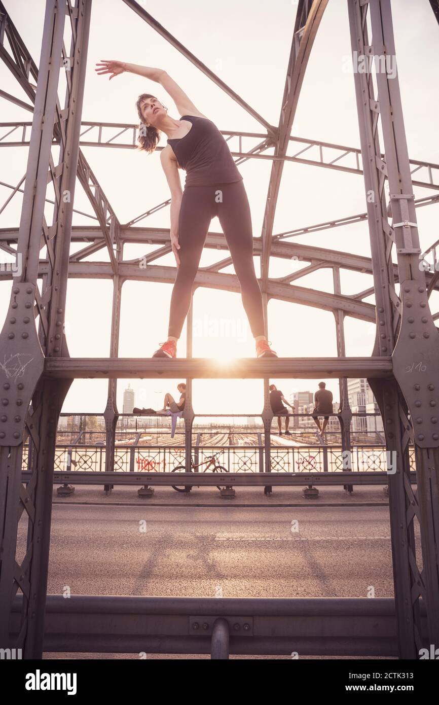 Femme s'exerçant sur un pont métallique au coucher du soleil Banque D'Images