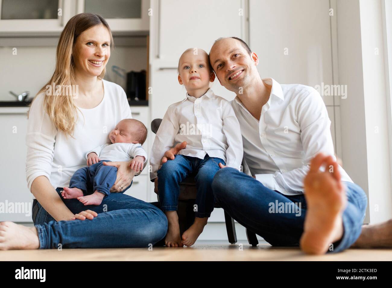 Parents souriants tenant des bébés garçons assis sur le sol accueil Banque D'Images