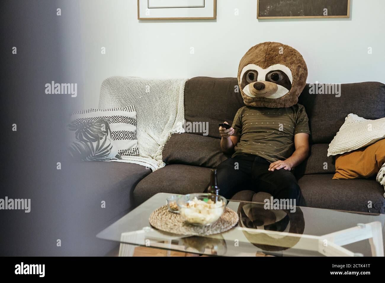 Homme adulte de taille moyenne portant un masque d'ours en peluche regardant la télévision séjour Banque D'Images