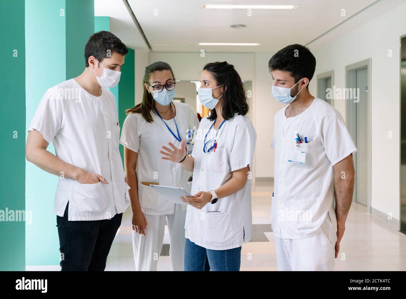 Les médecins portant des masques chirurgicaux discutant au-dessus d'une tablette numérique debout à l'hôpital Banque D'Images