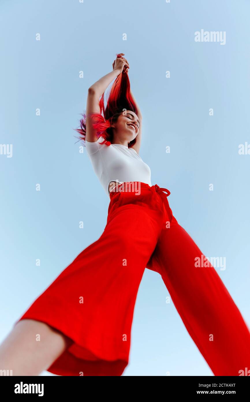 Jeune femme souriante tirant les cheveux rouges teints en se tenant debout contre le ciel dégagé Banque D'Images