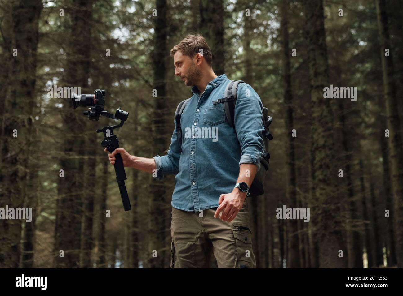 Homme filmant avec la caméra et la nacelle tout en se tenant contre les arbres en forêt Banque D'Images