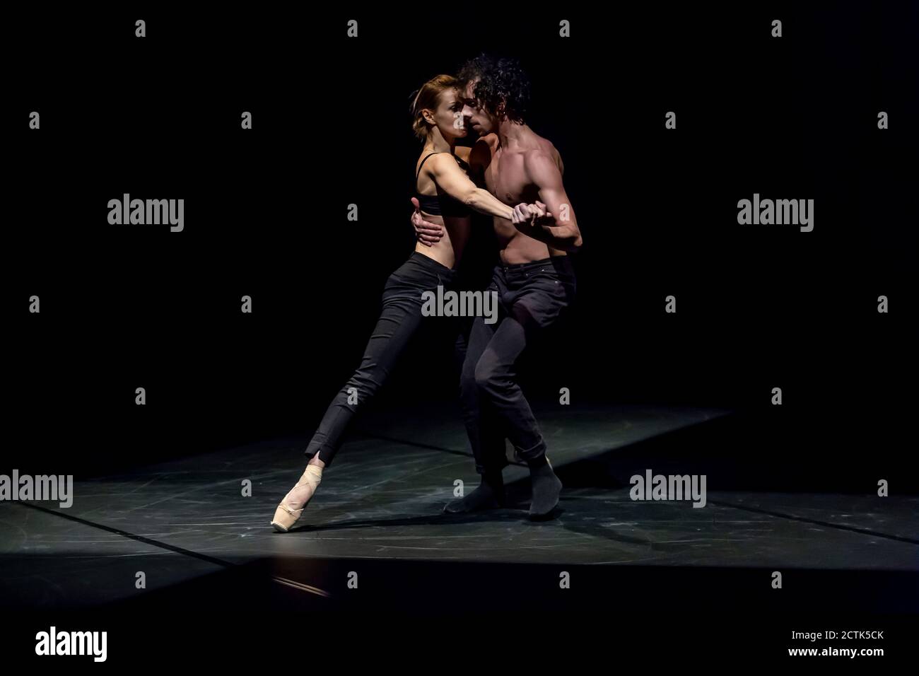 Danseuse féminine et masculine effectuant un ballet contemporain sur scène noire Banque D'Images
