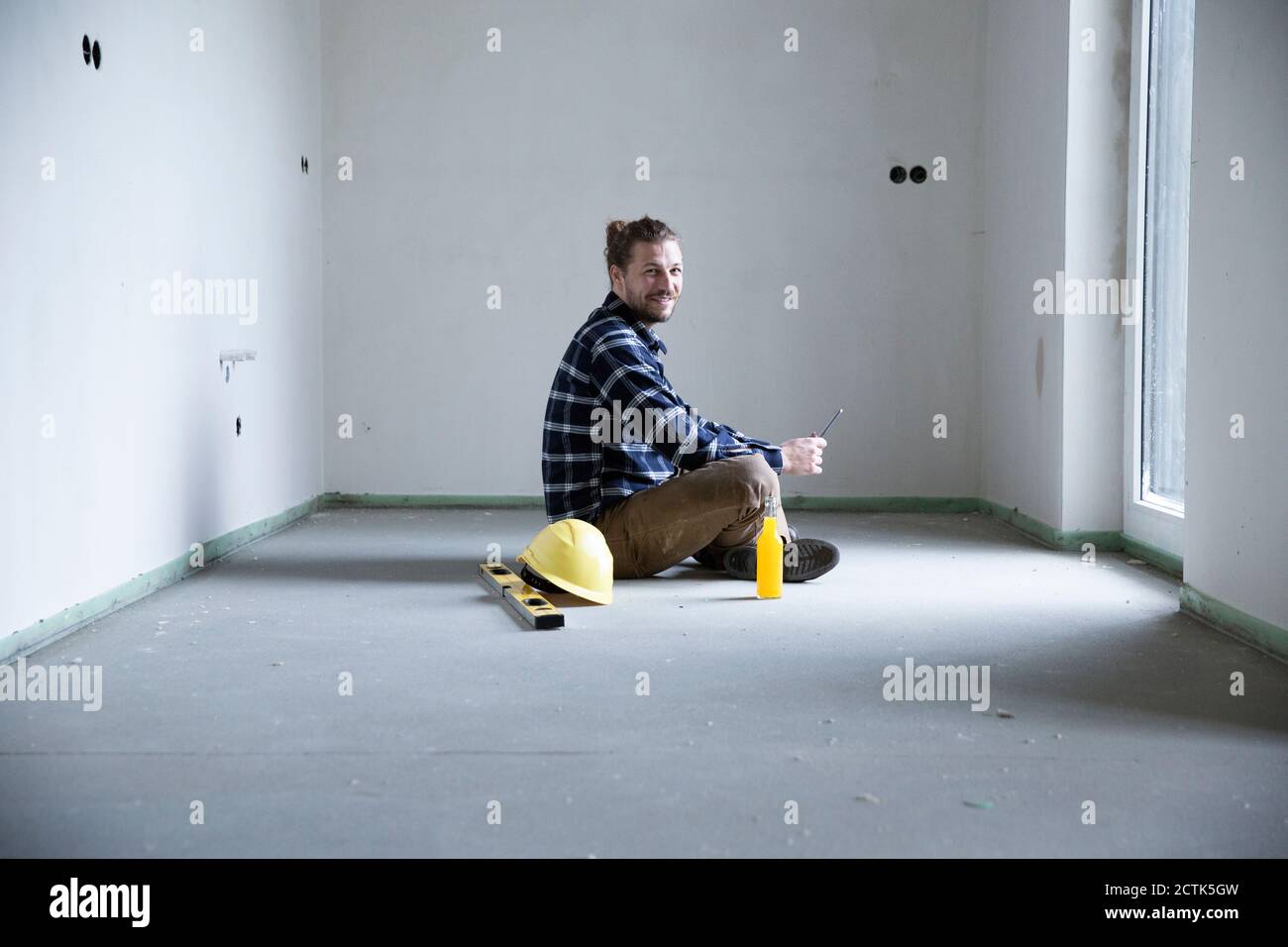 Travailleur de la construction assis sur le sol dans une maison vide lors de la construction site Banque D'Images