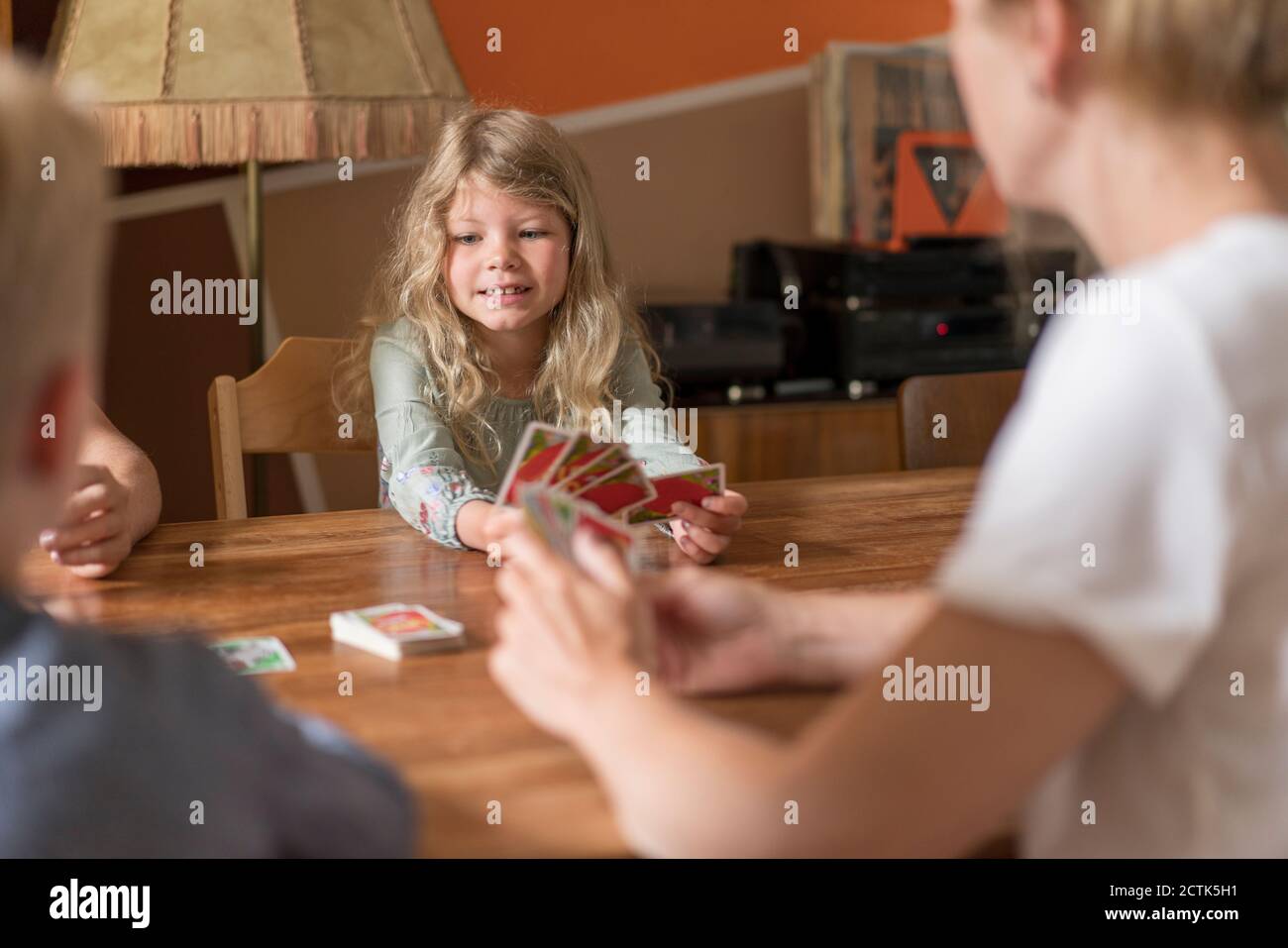 Mignonne blonde fille jouant des cartes avec la famille à la table à manger Banque D'Images