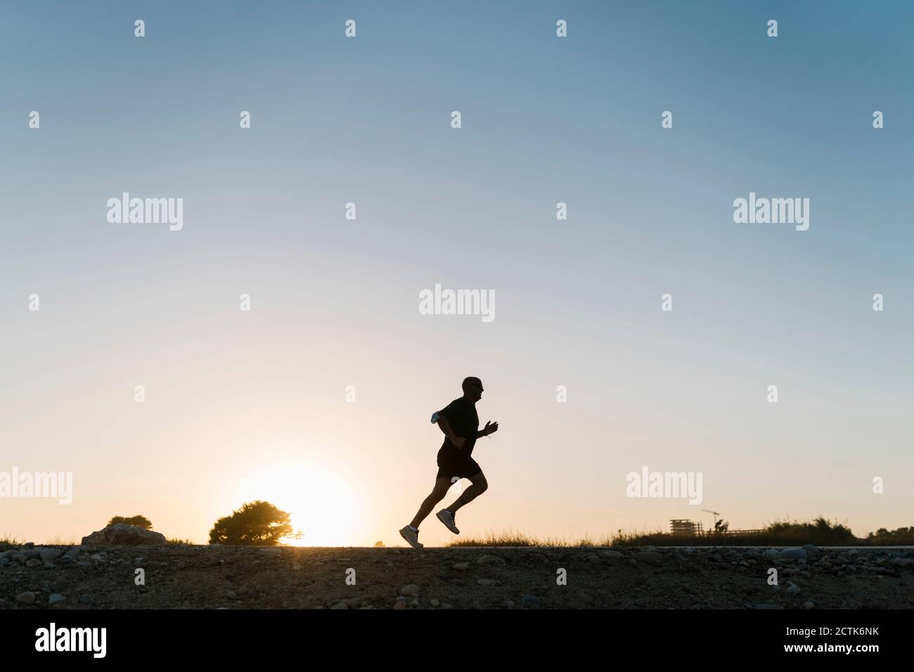 Silhouette d'athlète senior qui fait du jogging dans un ciel dégagé au coucher du soleil Banque D'Images