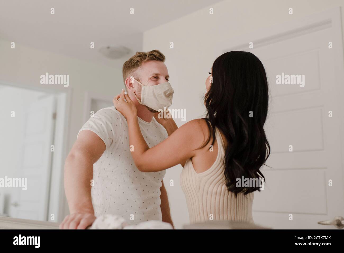Femme couvrant le visage du partenaire avec un masque de protection pendant COVID-19 Banque D'Images